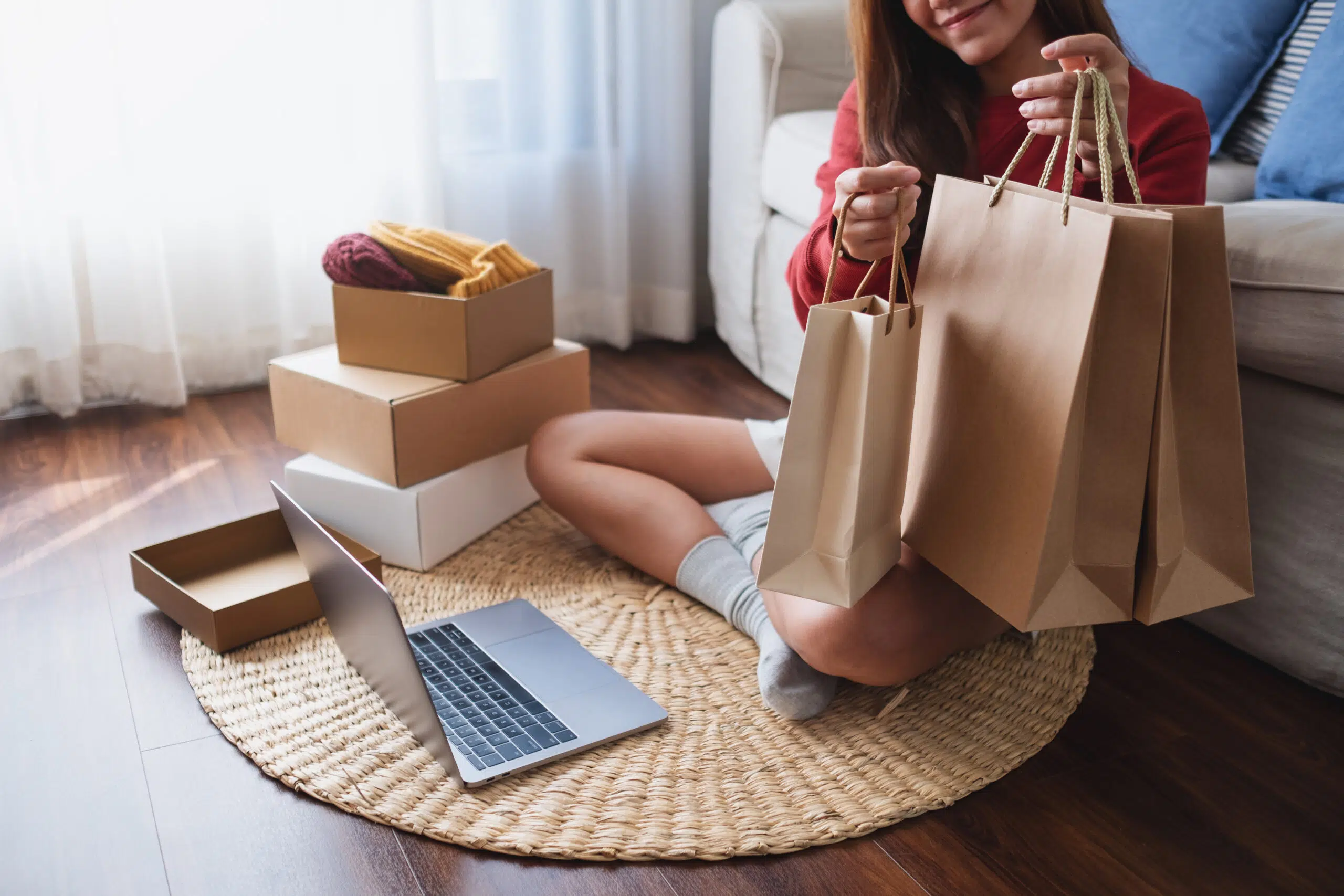A woman using laptop for online shopping , holding shopping bags and opening postal parcel box at home